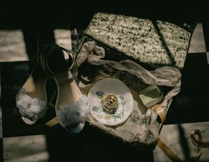 Vintage shoes and a teacup rest on a checkered surface with scattered papers in moody lighting.