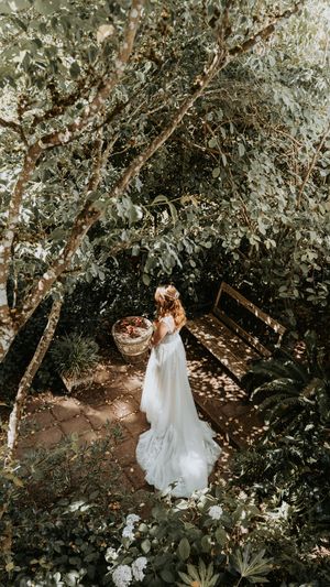 A romantic forest wedding scene with flowing white dresses captured in dappled sunlight through trees.