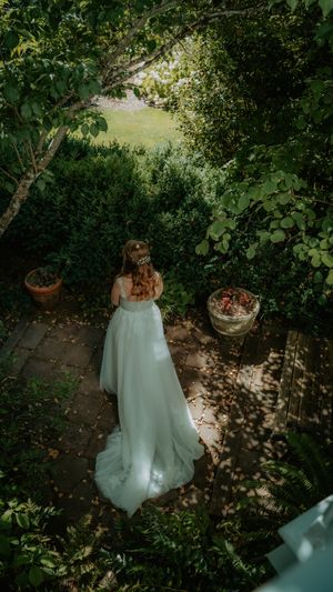 White wedding dress flowing in a lush garden setting with dappled sunlight filtering through trees.
