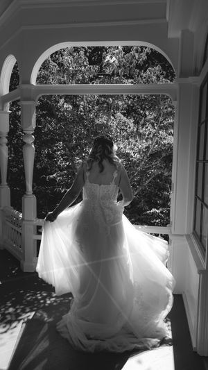 Flowing white wedding dress billowing in the breeze on an elegant white porch with arched columns.