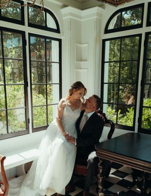 A romantic wedding moment in a bright corner room with large arched windows overlooking a garden.