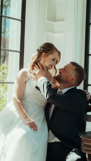 A romantic moment between newlyweds as they embrace in front of sunlit windows.