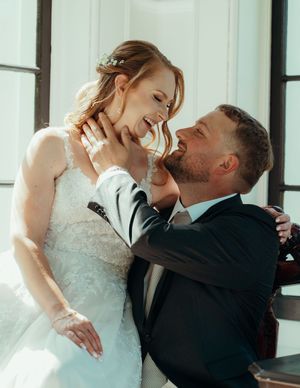 Romantic wedding moment captured in soft natural light against white interior backdrop.