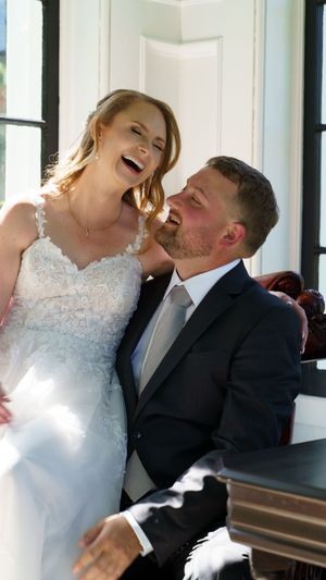 A joyful couple laughs together during their wedding photoshoot indoors.