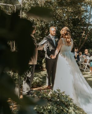 An outdoor wedding ceremony in a sunlit garden with lush greenery and white chairs.