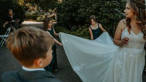 Wedding guests gather outdoors for a celebration with white floral decorations and greenery in the background.