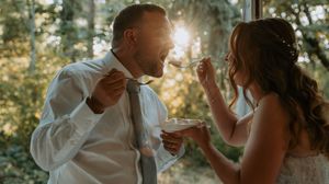A joyful wedding moment captured during cake tasting in golden sunlight.