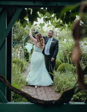 Wedding couple dances together in a lush garden setting with blooming flowers.