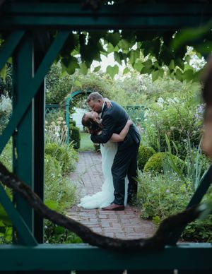 Wedding couple embracing in a garden setting framed by architectural elements.