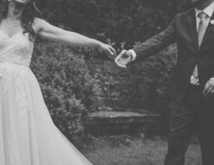 A black and white photo capturing a couple holding hands during their wedding ceremony in a garden setting.