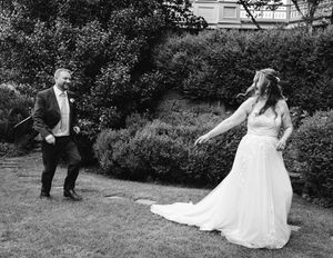 Wedding couple playfully dances and twirls in a black and white outdoor garden scene.