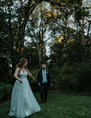 A couple dances together on a grassy hill surrounded by trees at sunset.