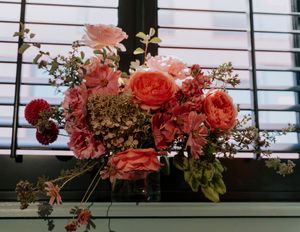 Pink and coral floral arrangements with roses and greenery decorate a white slatted wall backdrop.