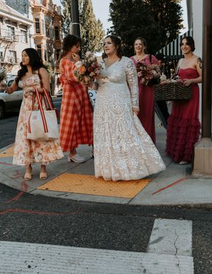 A bridal party in colorful dresses poses together on a street corner.