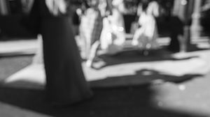 Black and white photo showing blurred silhouettes of people casting shadows on the ground.
