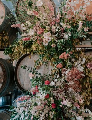 Lush floral arrangement with pink blooms and greenery decorating wine barrels in an event space.