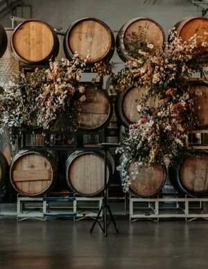 Rustic wooden wine barrels line a wall decorated with romantic floral arrangements in pink and white.