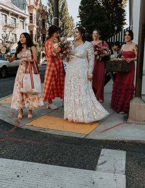 Wedding party in red and floral dresses posing together on a sidewalk during golden hour.