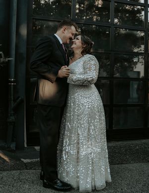 A couple shares an intimate dance moment in front of large windows at dusk.