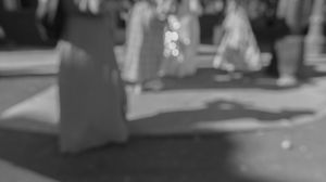 A black and white image shows a person walking down a city street at night with buildings in the background.