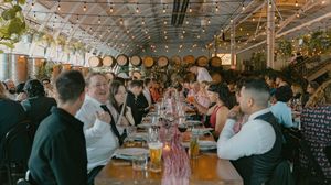 Wedding reception dinner in a rustic venue with string lights and long tables filled with guests.