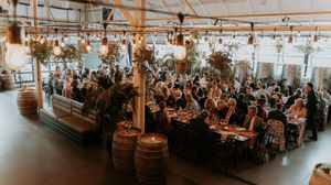 Panoramic view of a rustic winery event space with wooden barrels and string lights.