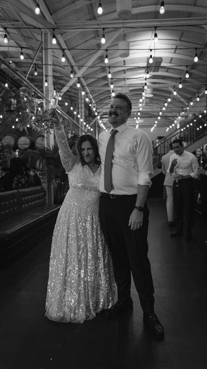 A couple dances under string lights in a reception venue, with the bride wearing a sparkly gown.