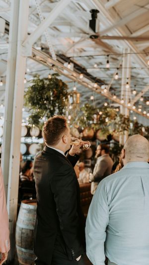 Guests mingling at an indoor reception with rustic decor and wooden barrels visible in the background.