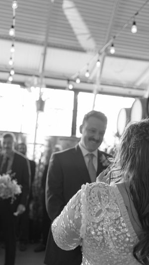 A candid black and white wedding moment under string lights showing a sparkly lace dress detail.