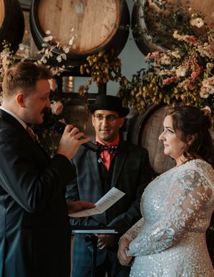 A wedding ceremony in a rustic venue with floral decorations and wine barrels.