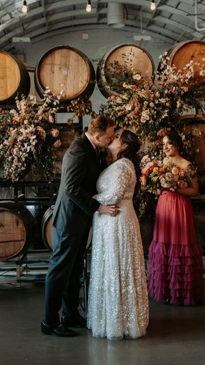 A wedding first dance in a winery with wine barrels and pink floral arrangements.