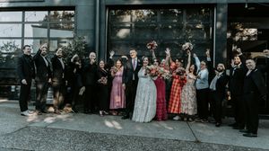 Large wedding party group photo taken outside a venue with formal attire.