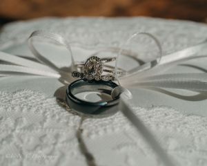 A close-up macro shot of a diamond engagement ring resting on white lace fabric with soft lighting.