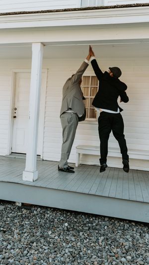 Wedding party members playfully peek around the corner of a white porch during a photo session.
