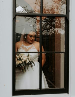 A bride in a white dress poses by a window pane in an artistic wedding photography composition.