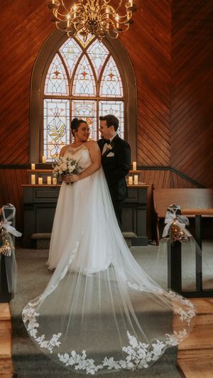A romantic wedding scene in a chapel with stained glass windows and a dramatic flowing veil with lace details.