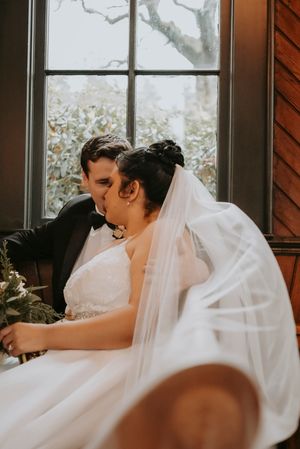 A bride in a white wedding dress and veil reclines on a couch by a window during a quiet moment.