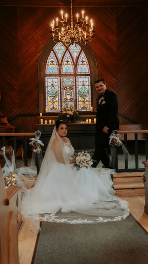 A wedding ceremony in a chapel with stained glass windows, wooden walls and an elegant chandelier.