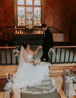 A romantic wedding scene in a chapel with stained glass windows and decorative white bows on pews.
