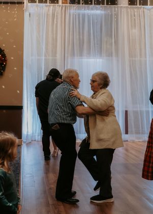 Elderly couple dancing together at a wedding reception in front of white curtains and string lights.
