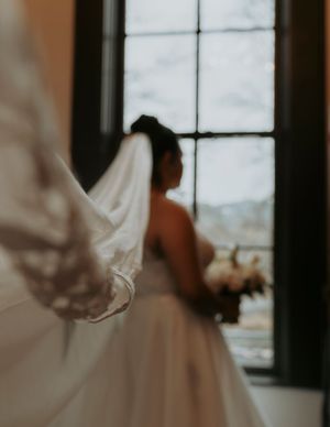 A flowing white wedding dress veil catches the light through windows in an elegant indoor setting.