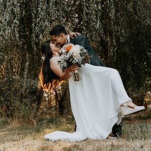 A romantic wedding couple shares tender moments in a rustic outdoor setting with natural lighting and foliage.