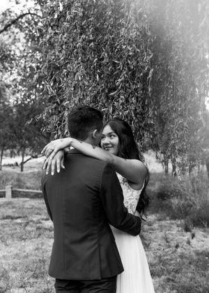 A couple embraces in a romantic outdoor photoshoot with soft natural lighting and trees in the background.