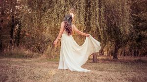 A bride in a flowing white dress walks through a sunlit autumn forest during a romantic outdoor photoshoot.