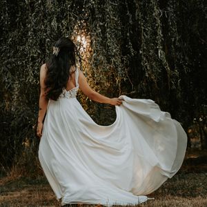 Flowing white wedding dress twirls gracefully in a forest setting during golden hour sunlight.