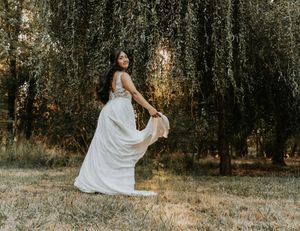 A person in a flowing white dress spins gracefully in a sun-dappled forest setting during golden hour.