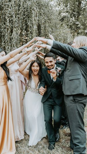 Wedding party in formal attire strikes playful dabbing pose together outdoors in nature setting.