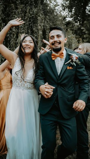 Wedding party laughs together outdoors while wearing formal attire with bridesmaids in yellow dresses.