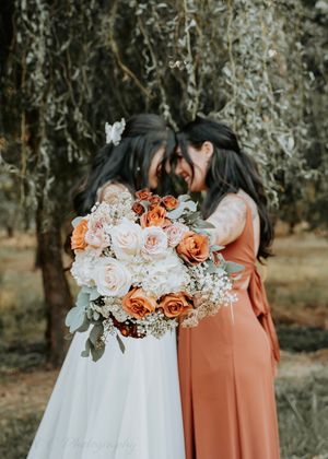 Beautiful peach and white floral bouquets with roses and greenery against a rustic outdoor backdrop.