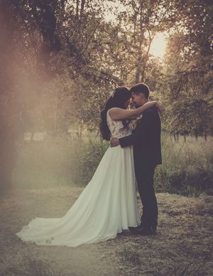 A sunset wedding portrait with a flowing white dress and golden light filtering through trees.